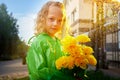 Cute little blonde girl in green raincoat with yellow flowers on a green lawn under rain drops in a summer sunny day Royalty Free Stock Photo
