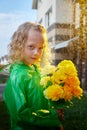 Cute little blonde girl in green raincoat with yellow flowers on a green lawn under rain drops in a summer sunny day Royalty Free Stock Photo