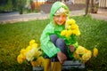 Cute little blonde girl in green raincoat with yellow flowers on a green lawn under rain drops in a summer sunny day Royalty Free Stock Photo