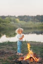 Cute little blonde girl roasting and eating marshmallows on stick at bonfire