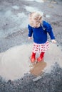 Cute little blonde girl wearing red rain boots jumping into a puddle Royalty Free Stock Photo