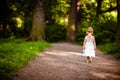 Cute little blonde girl in a white dress walking down the path i