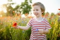 Cute little boy admiring poppy and knapweed flowers in blossoming poppy field on sunny summer day