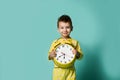 Cute little boy with alarm clock, on blue. Funny kid pointing at alarm clock at morning.