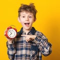 Cute little boy with alarm clock,isolated on yellow. Funny kid pointing at alarm clock at 7 o `clock at morning. Excited boy overs