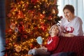 Cute little boy with big sweet candy sitting on sofa near a Christmas tree. Child is looking on his mother or grandmother. Royalty Free Stock Photo