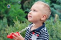 Cute little boy with blond hair and blue eyes blows bubbles from plastic toy and looks at them excitingly. Royalty Free Stock Photo