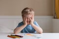 Cute little boy with blond hair draws colored pencils. He put his hands on his face and thinking about something Royalty Free Stock Photo