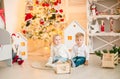 Cute little boy with blond hair plays with little girl in a bright room decorated with Christmas garlands