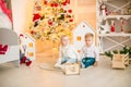 Cute little boy with blond hair plays with little girl in a bright room decorated with Christmas garlands