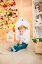 Cute little boy with blond hair plays with toys in a bright room decorated with Christmas garlands near the Christmas tree.