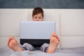 Cute little boy child Laying on the bed at home looking at laptop computer screen. Selective focus on bare foot Royalty Free Stock Photo