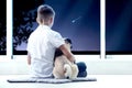 Cute little boy with dog sitting near window and looking at shooting star in night sky Royalty Free Stock Photo