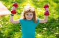 Cute little boy doing exercises with dumbbells in green park. Portrait of sporty child with dumbbells. Happy child boy Royalty Free Stock Photo