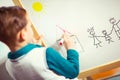 Cute little boy drawing on white board with felt pen and smiling Royalty Free Stock Photo