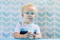 Cute little boy drinking milk with funny glasses straw.
