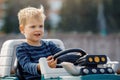 Cute little boy driving big electric toy car with steering wheel and having fun outdoors Royalty Free Stock Photo