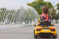 Cute little boy driving children`s car near fountain on city street, back view. Space for text Royalty Free Stock Photo