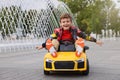 Cute little boy driving children`s car near fountain on city street. Space for text Royalty Free Stock Photo