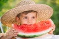 Cute little boy eating slice of juicy watermelon sitting on natural green garden background. Adorable kid in straw hat Royalty Free Stock Photo