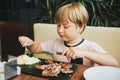 Cute little boy eating steak in restaurant