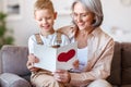 Cute little boy grandson congratulating smiling grandmother and giving handmade greeting card