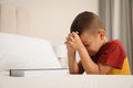 Cute little boy with hands clasped together saying bedtime prayer over Bible at home. Space for text