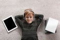 Cute boy with headphones and tablet listening to audiobook on floor indoors, flat lay