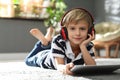 Cute boy with headphones and tablet listening to audiobook at home