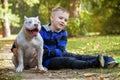 Cute little boy with his friend, five months old puppy of American Bully dog of white color, sitting in autumn park and smiling. Royalty Free Stock Photo