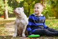 Cute little boy with his friend, five months old puppy of American Bully dog of white color, sitting in autumn park and smiling. Royalty Free Stock Photo