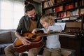 Cute little boy and his handsome father are playing guitar and smiling at home Royalty Free Stock Photo