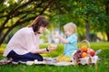 Cute little boy with his young mother opening nicely wrapped gift during picnic in sunny park