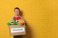 Cute little boy holding donation box with soft toys near yellow brick wall, space for text Royalty Free Stock Photo