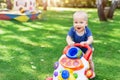 Cute little boy learning to walk with walker toy on green grass lawn at backyard. Baby laughing and having fun making first step a Royalty Free Stock Photo