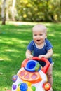 Cute little boy learning to walk with walker toy on green grass lawn at backyard. Baby laughing and having fun making first step a Royalty Free Stock Photo