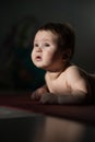 A cute little boy lies on his forearms on the floor. Vertical photo.