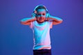 Cute little boy, listening music in headphones and holds hands on it in mixed neon light against blue background.