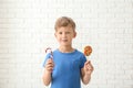 Cute little boy with lollipop and candy cane near white brick wall