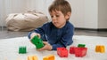 Cute little boy lying on soft carpet and playing with colorful toy blocks. Concept of child education and games at home Royalty Free Stock Photo