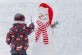 Cute little boy made and draws smile on face snowman in winter Park Royalty Free Stock Photo