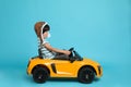 Cute little boy in pilot hat driving children`s electric toy car on light blue background Royalty Free Stock Photo