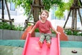 Cute little boy playfull on red plastic slide in playground. Children boy having fun on outdoors playground on sunny summer day. Royalty Free Stock Photo