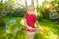 Cute little boy is playing with big bubbles outdoor. Child is blowing big and small bubbles simultaneously Royalty Free Stock Photo