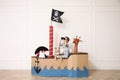 Cute little boy playing with binoculars in pirate cardboard ship near white wall indoors Royalty Free Stock Photo