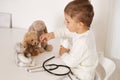 Cute little boy playing doctor at home and curing plush toy. Sweet toddler child plays indoor. Having fun. Kids and Royalty Free Stock Photo