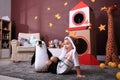 Cute little boy playing on floor near cardboard rocket at home. Child`s room interior