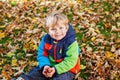 Cute little boy playing with maple leaves outdoors. Happy child walking in autumn park. Toddler baby boy wears trendy Royalty Free Stock Photo