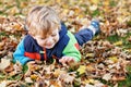 Cute little boy playing with maple leaves outdoors. Happy child walking in autumn park. Toddler baby boy wears trendy Royalty Free Stock Photo