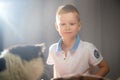 Cute little boy playing with a white and black cat in photo studio with white fabric background. Concept of friendship